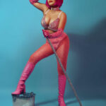 Burlesque star Cleopantha in pink, holding a mop and with one foot on a metal bucket.